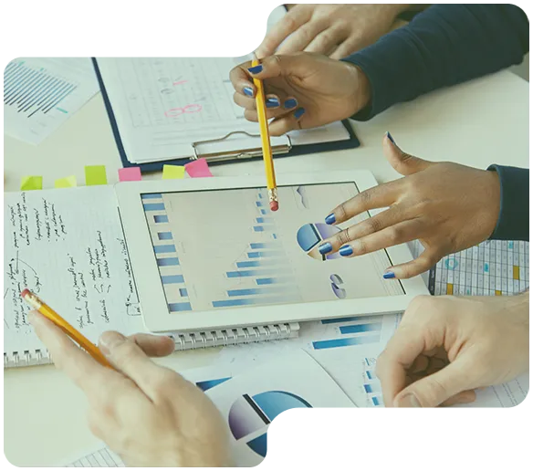 Personer som analyserar stapeldiagram och cirkeldiagram på surfplatta och papper vid ett skrivbord.