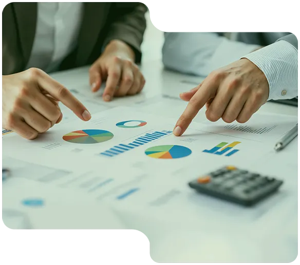 Två personer pekar på färgglada cirkeldiagram och stapeldiagram på ett bord med räknare.