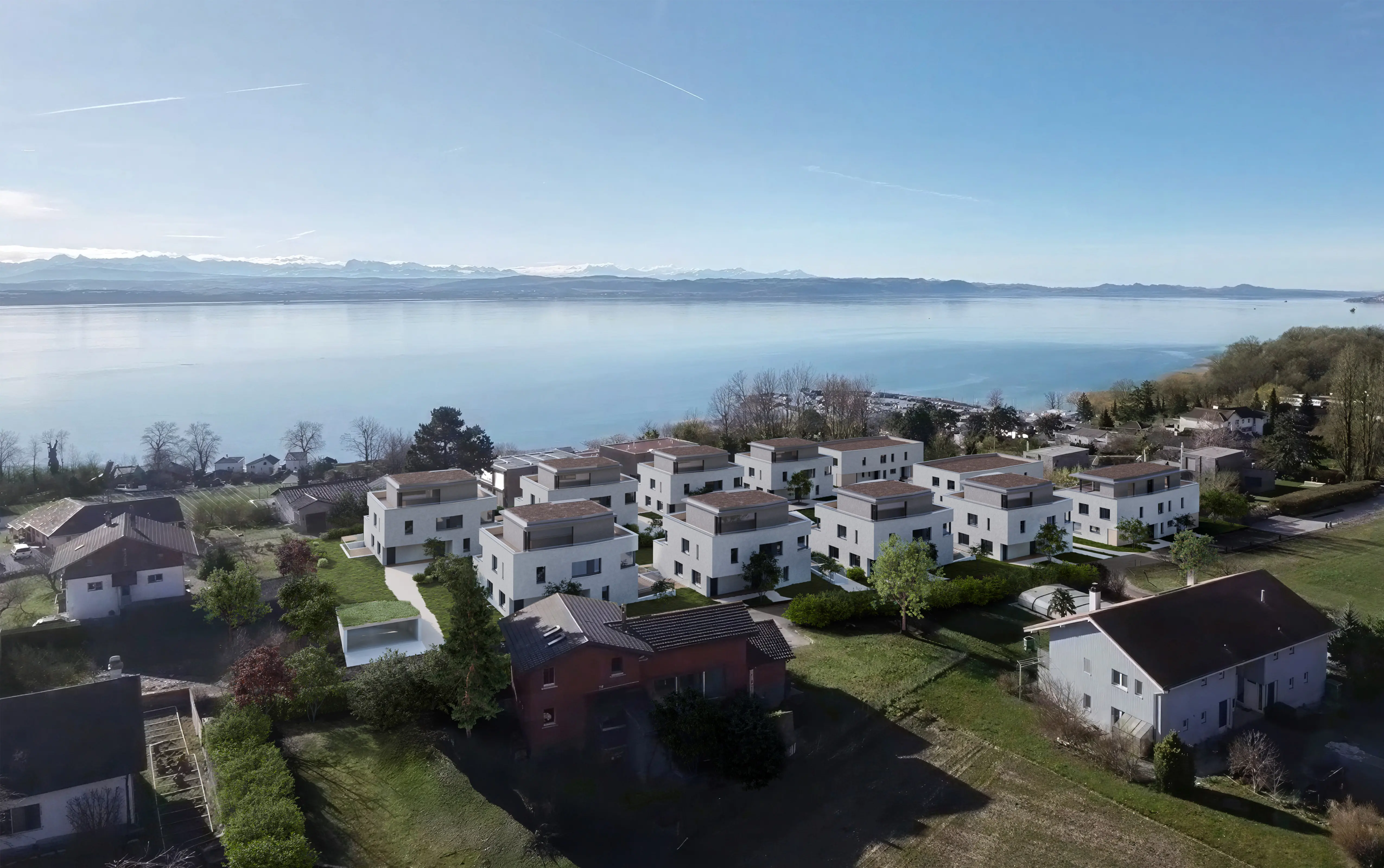 Vue aérienne d'un lotissement moderne avec des maisons blanches à toit plat près d'un grand lac et de montagnes en arrière-plan par temps clair.