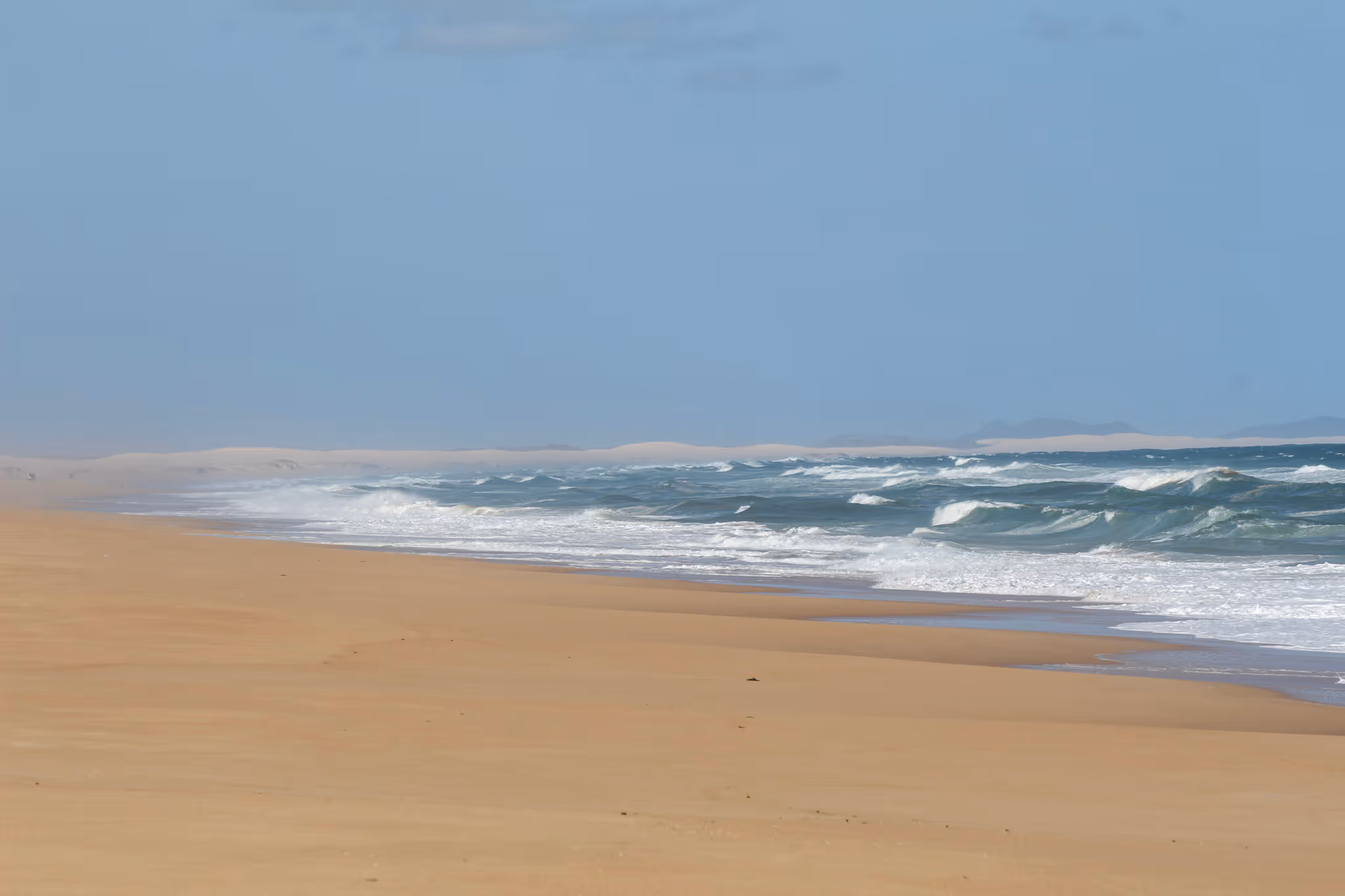 Wide sandy beach with ocean waves crashing under a clear blue sky.