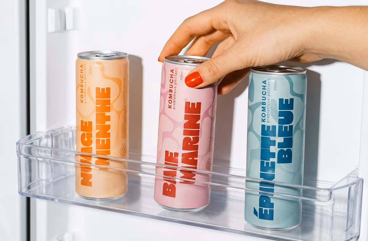 image generated by adobe fire fly - Hand with red nail polish grabbing pink kombucha can labeled Baie Marine from fridge door shelf.