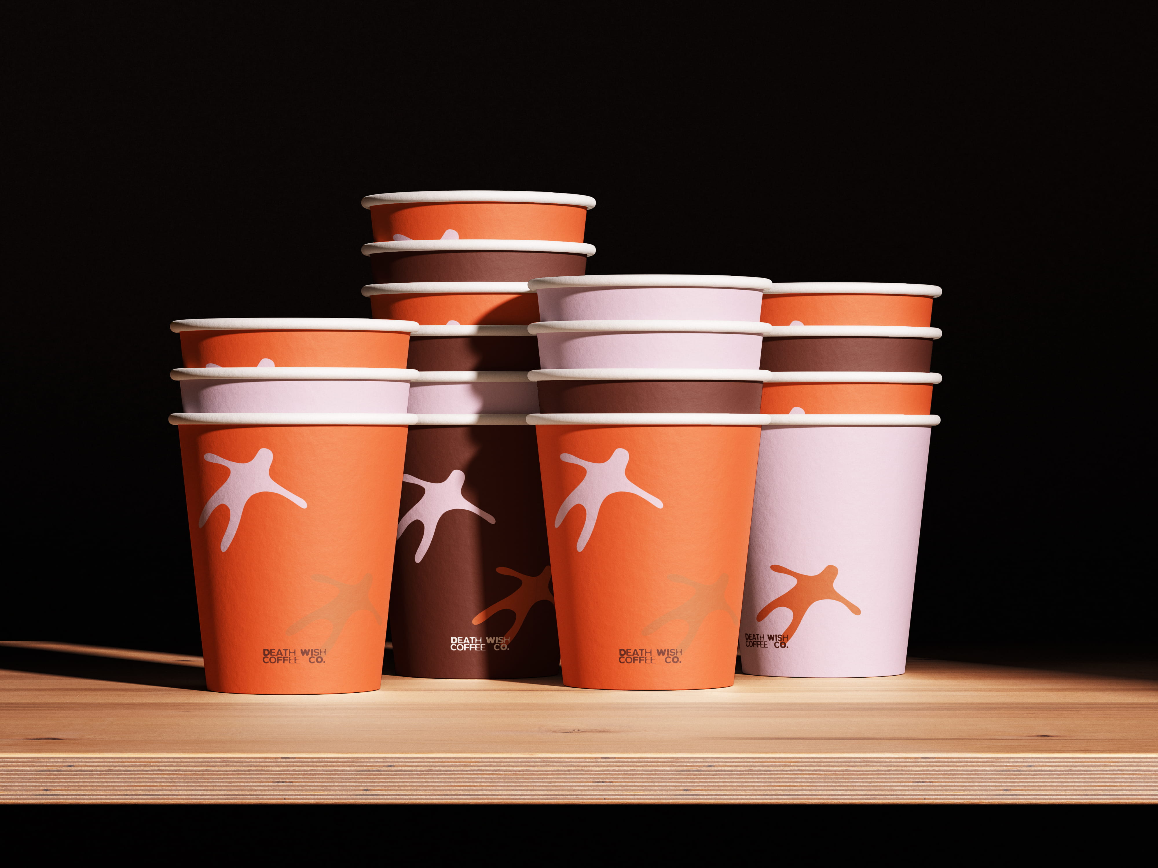 mockup found on magnific -Stacked orange, brown, and pink DEATH WISH COFFEE paper cups on a wooden surface with black background.