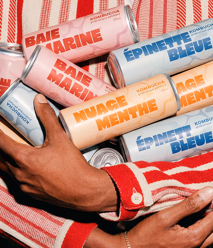 Image generated by adobe firefly - Person holding multiple colorful kombucha cans labeled Baie Marine, Nuage Menthe, and Épinette Bleue.