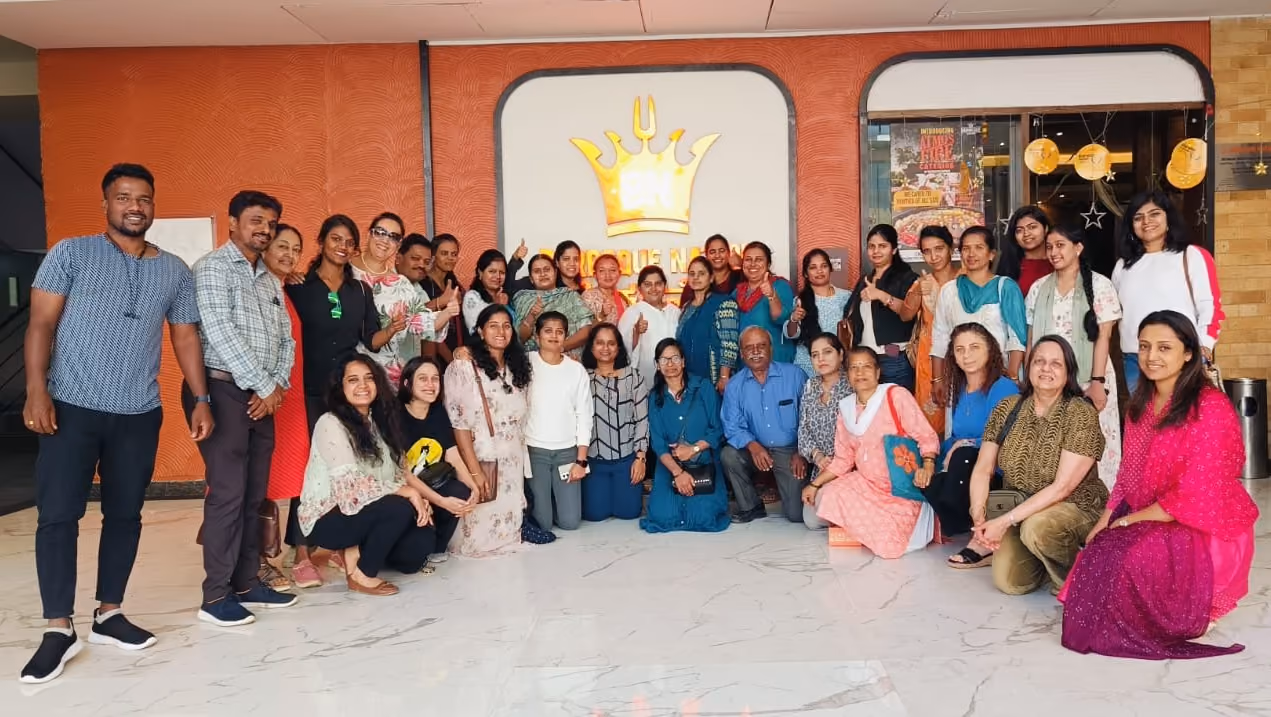 Group of smiling people posing together indoors in front of a wall with a crown logo.