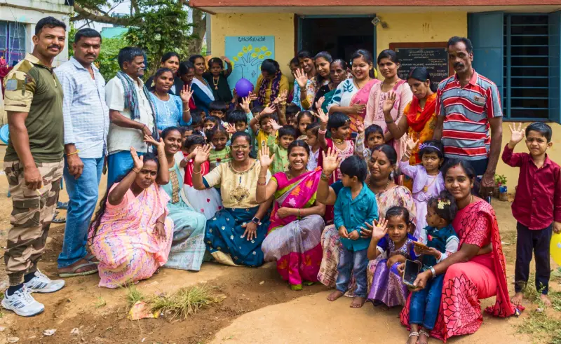 Group of diverse adults and children waving and smiling outdoors in front of a building.
