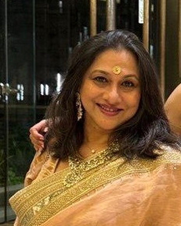 Woman smiling, wearing a gold embroidered saree with matching earrings and a decorative bindi.