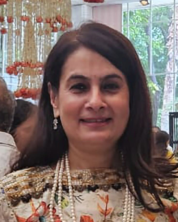 Woman smiling, wearing a gold embroidered saree with matching earrings and a decorative bindi.