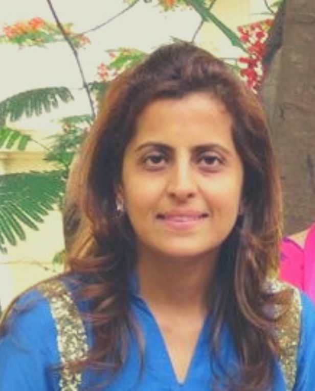 Woman smiling, wearing a gold embroidered saree with matching earrings and a decorative bindi.
