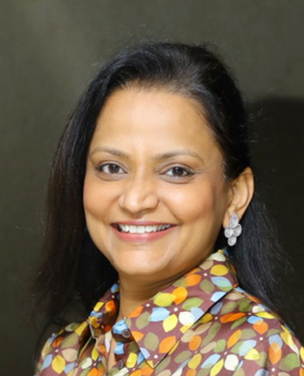 Woman smiling, wearing a gold embroidered saree with matching earrings and a decorative bindi.