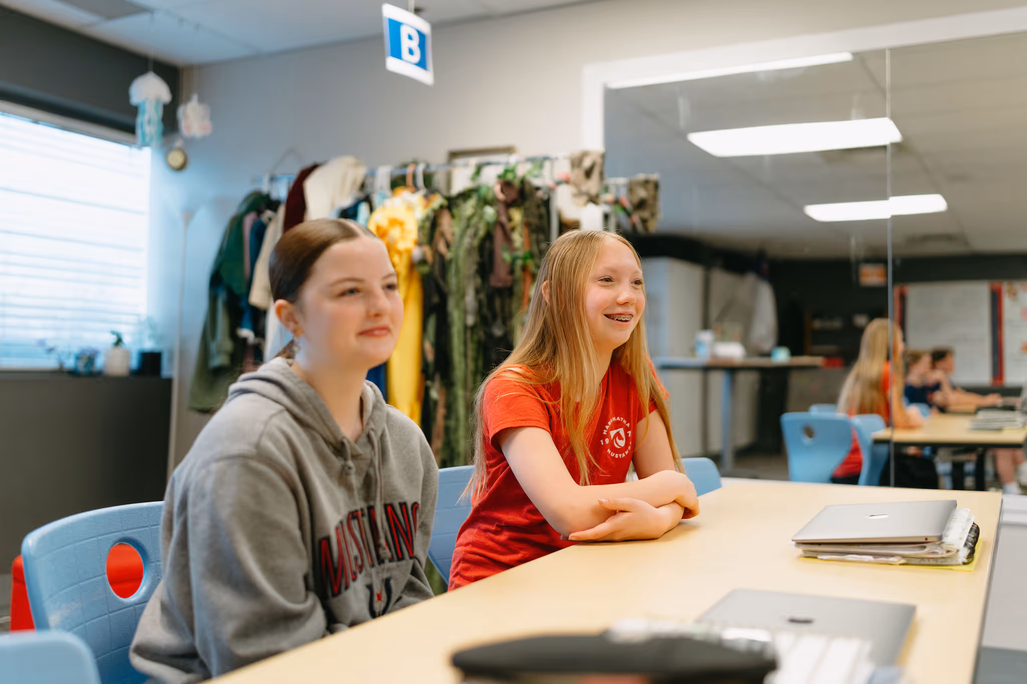Two middle school girls smiling and sitting together at a classroom table