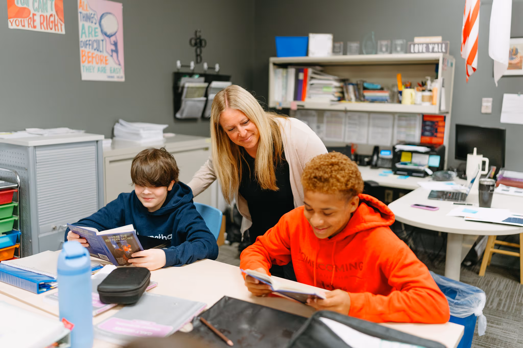 Teacher assisting middle school students with coursework at a desk