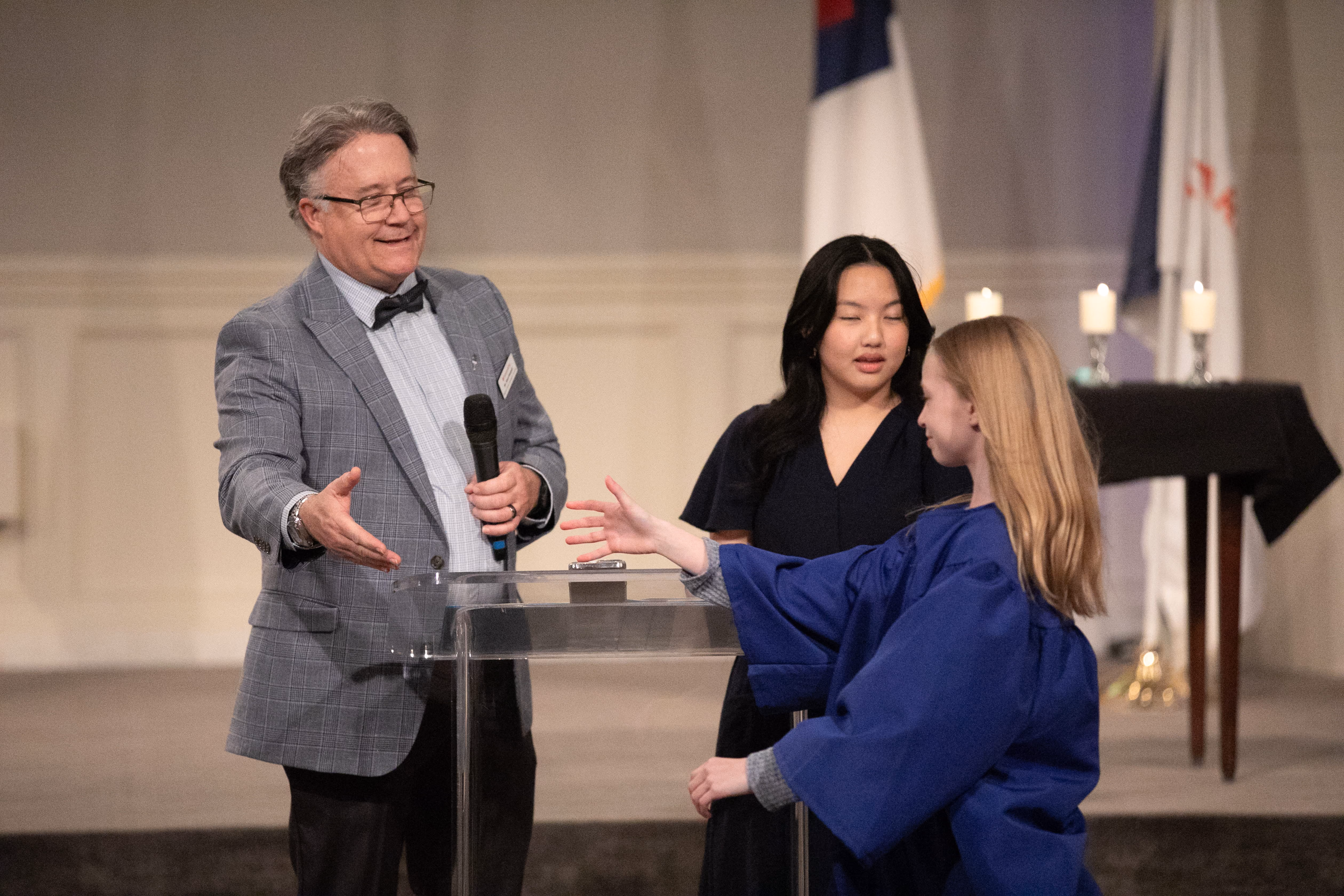 School administrator presenting an NJHS induction award to a student on stage