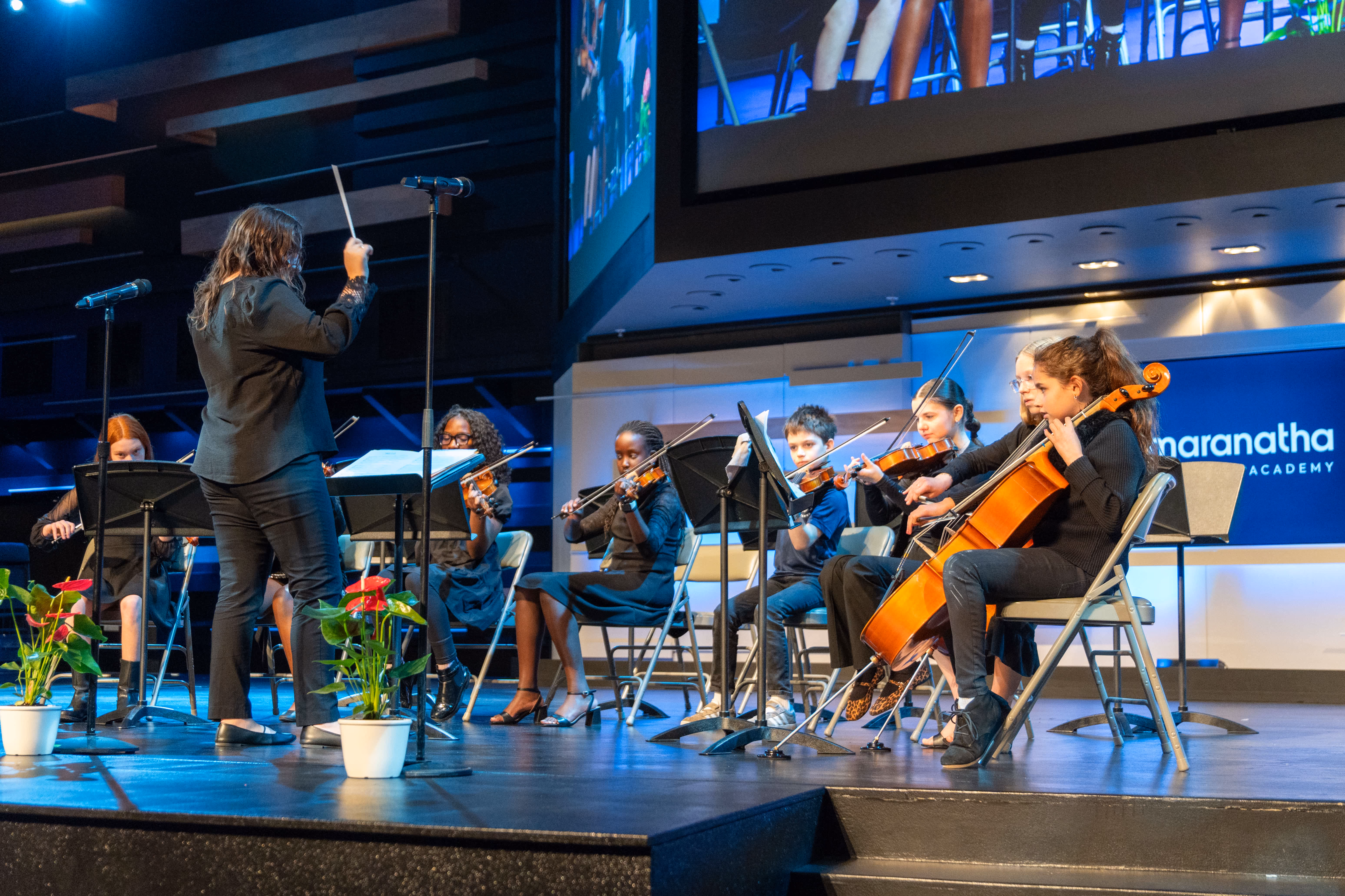 Orchestra conductor leading middle school strings and ensemble performers on stage