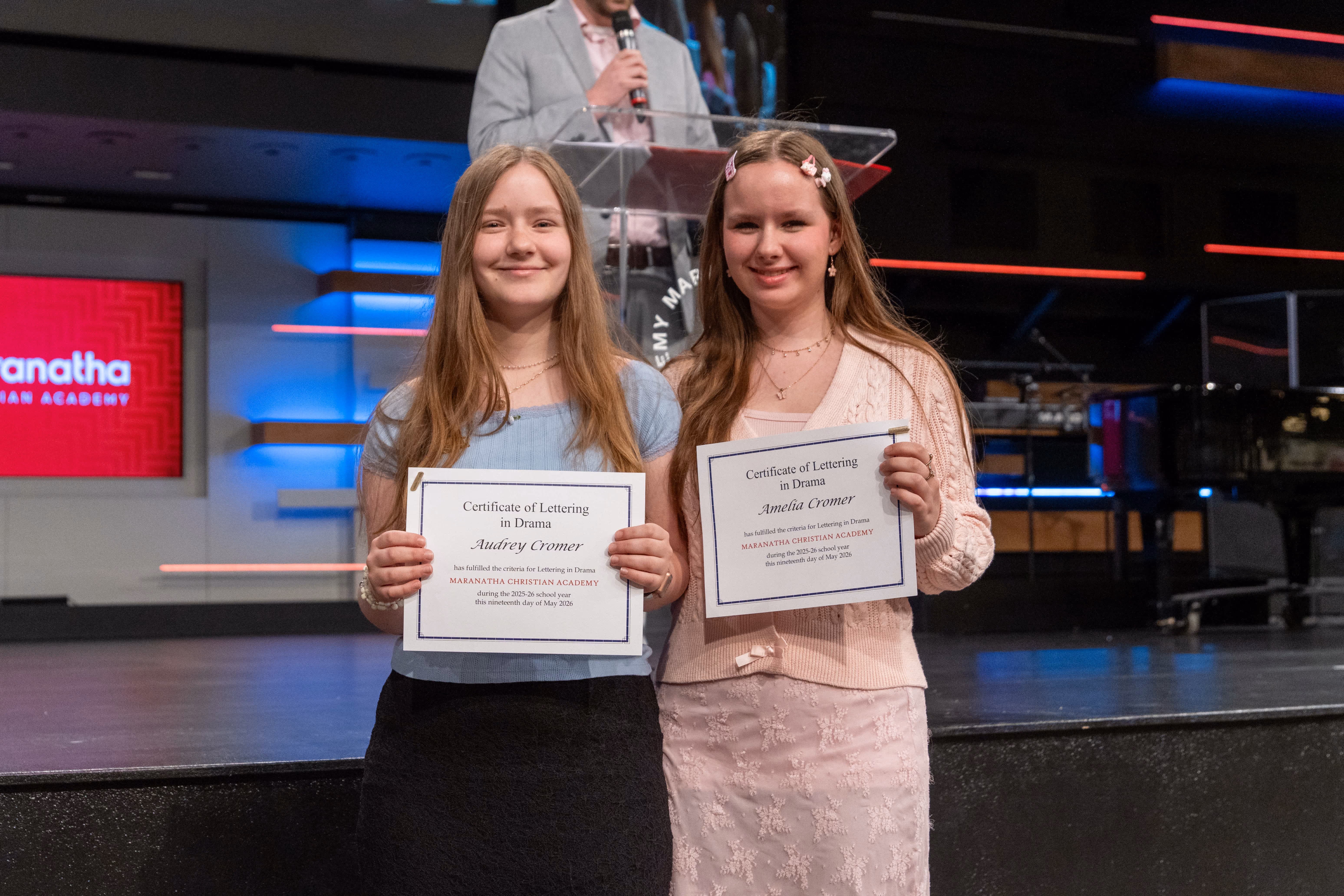 Two middle school girls smiling on stage holding academic certificates