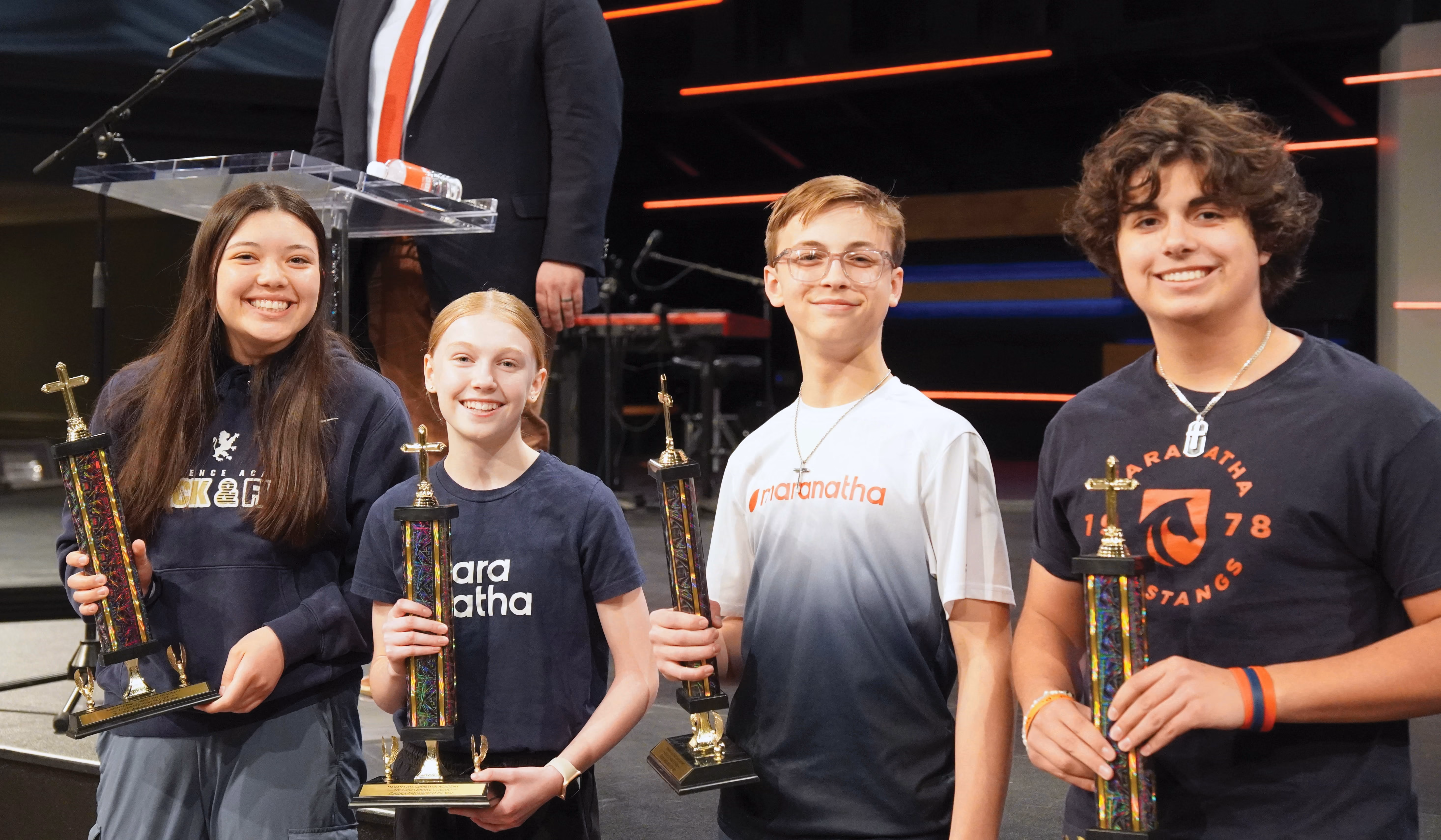 Middle school boy and girl smiling on stage holding Christian Ambassador trophies