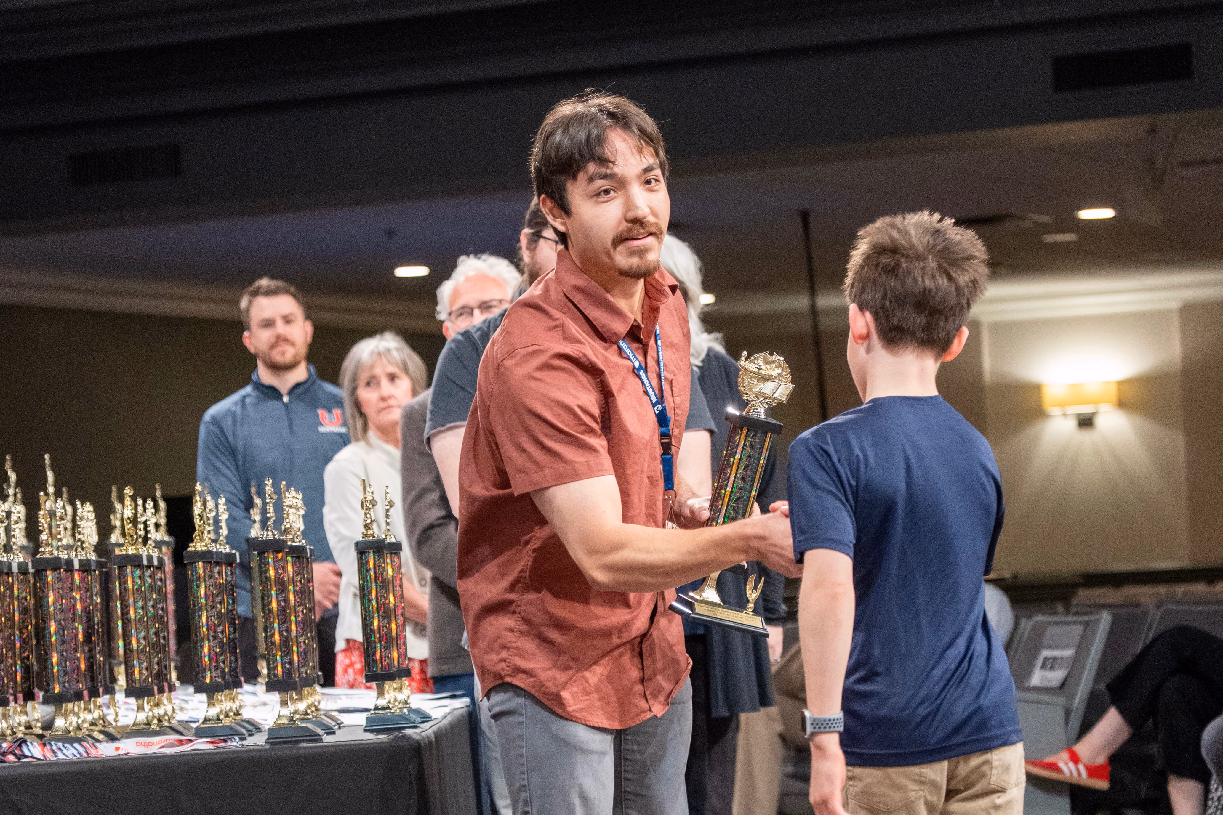 Teacher presenting an academic award trophy to a middle school boy on stage