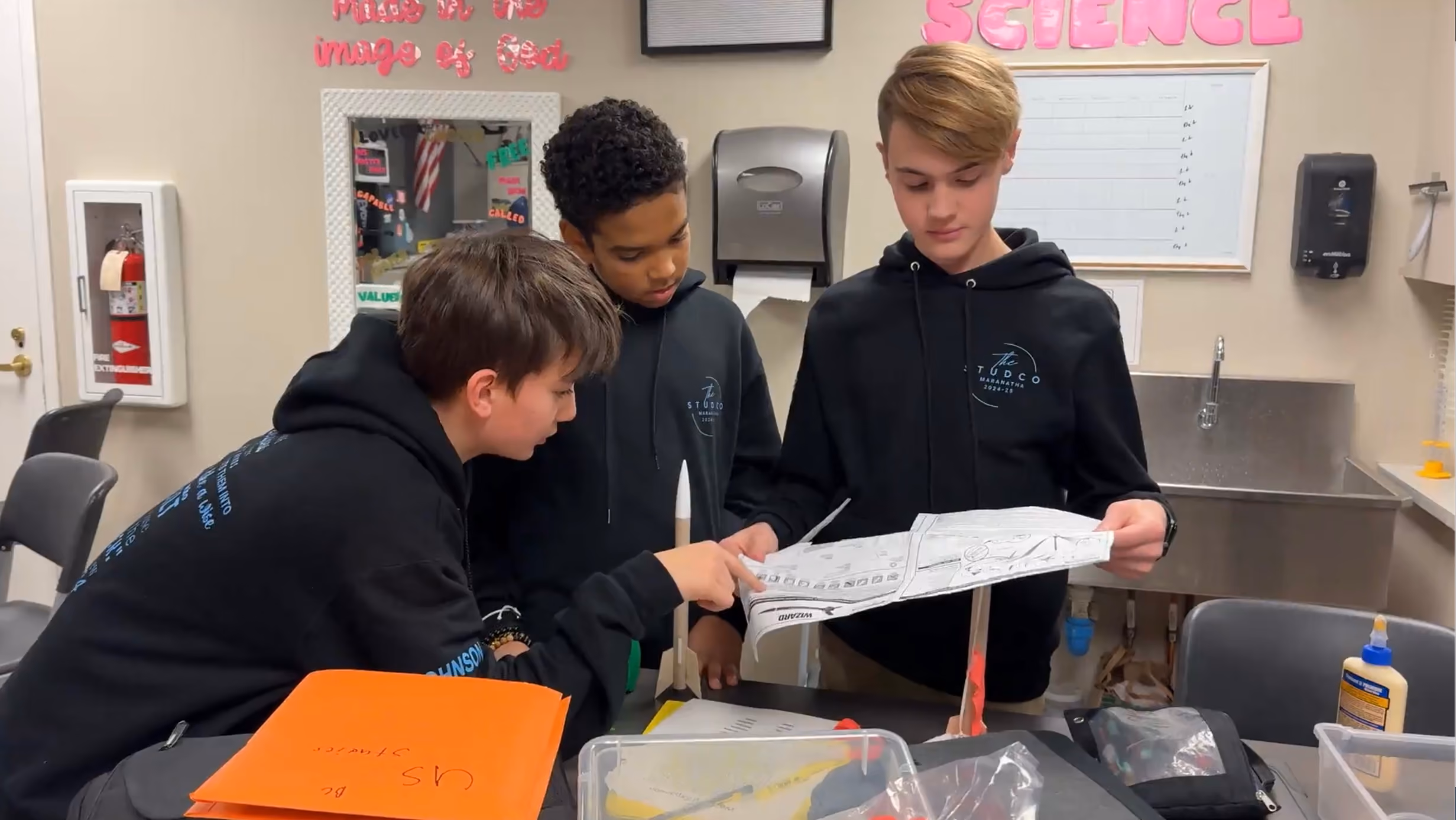 Students examining blueprints and constructing a model rocket in class