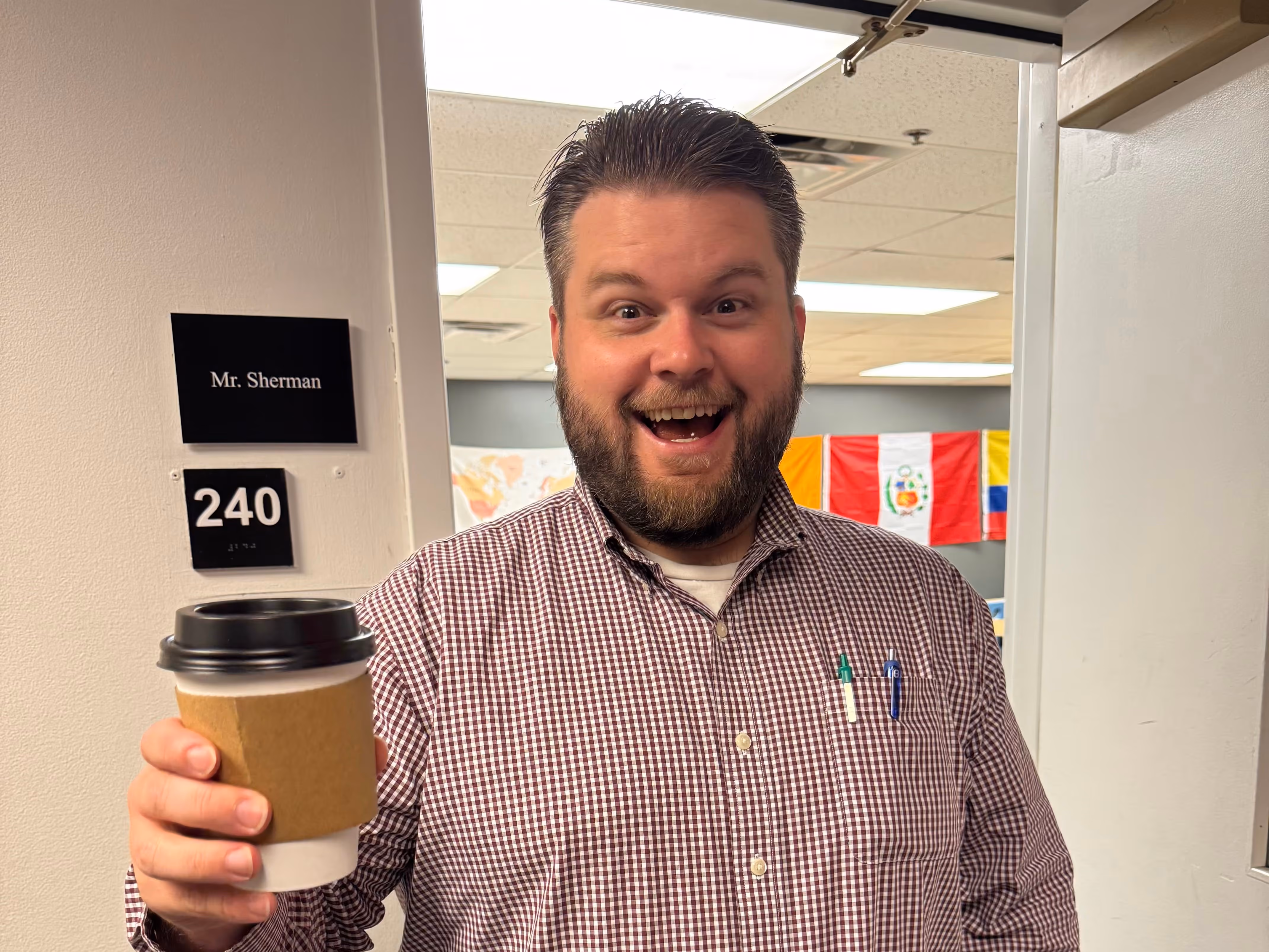 Male teacher smiling while holding a coffee cup in the school hallway