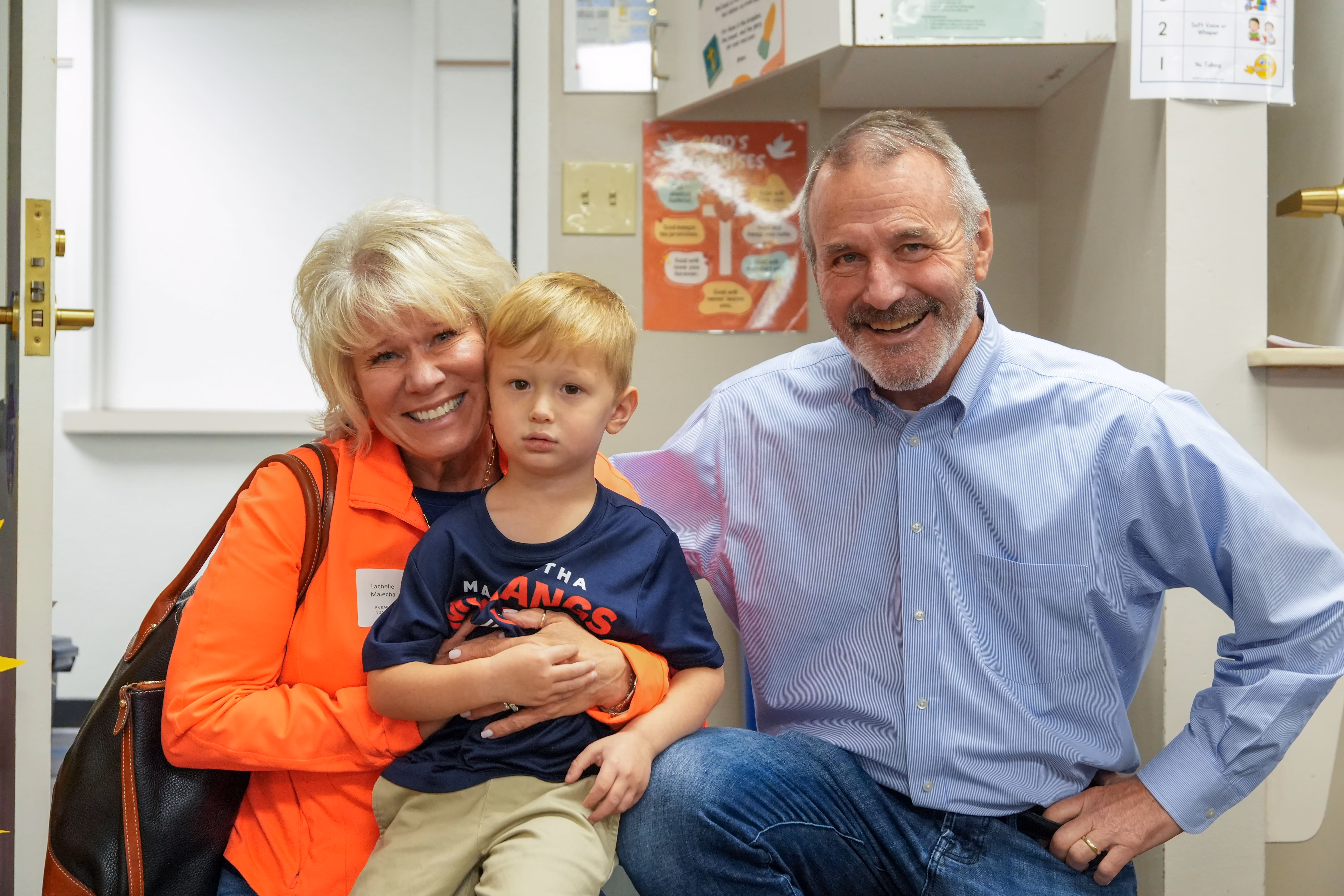 Two grandparents smiling warmly as they pose with their young grandson during a school event.
