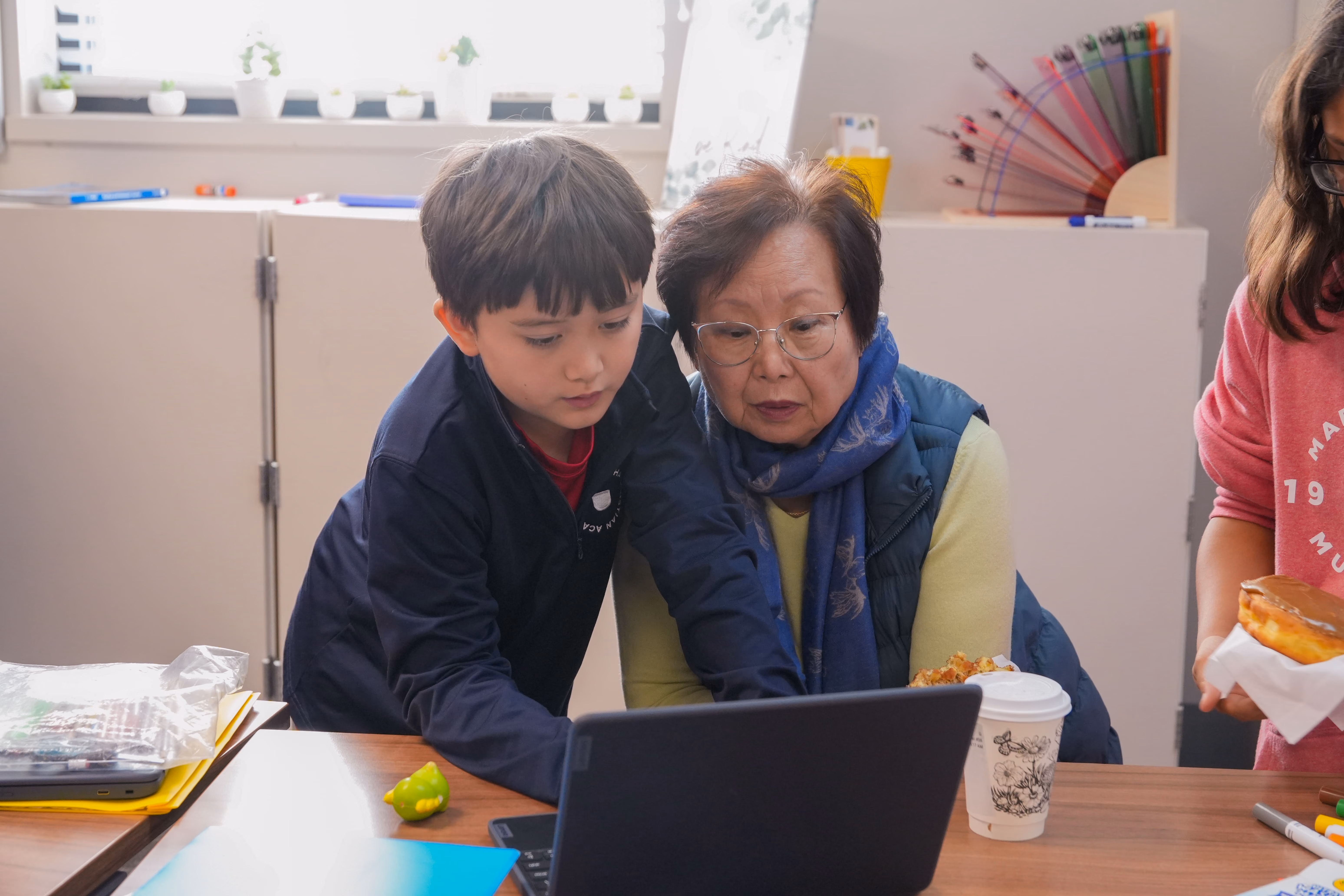 A young male student and his grandmother looking attentively at a laptop screen together.