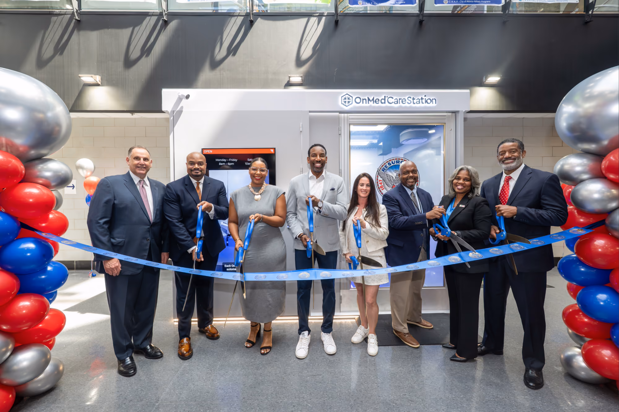 Community leaders cutting a ribbon at an OnMed CareStation™ grand opening with balloon arches on either side