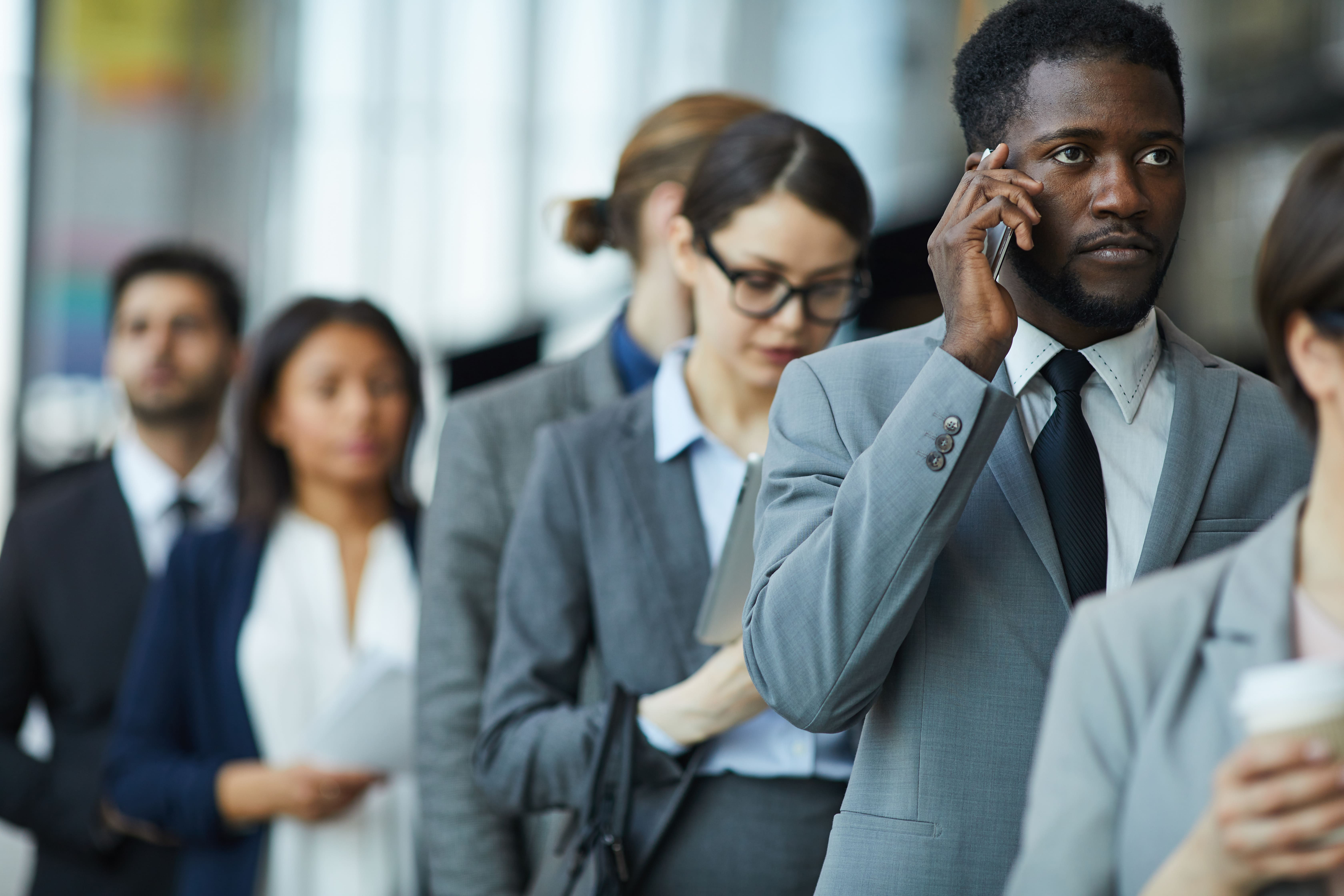 Diverse group of business professionals in modern office environment with focus on businessman on phone call, representing busy workplace wellness.