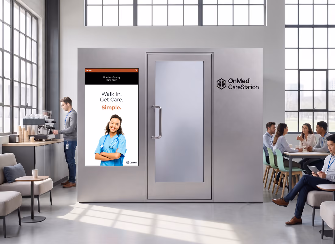 OnMed CareStation® in gray in an office break room, with a video screen displaying "Walk In. Get Care. Simple." near people at a table