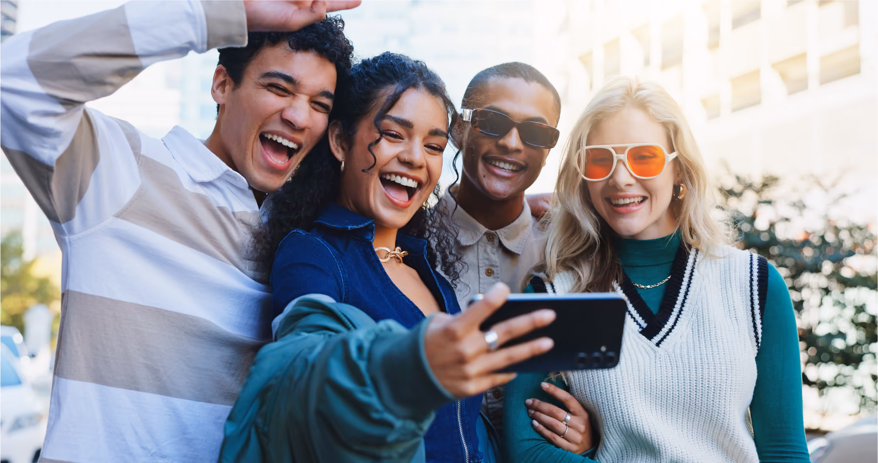 Group of young friends laughing while taking a selfie outdoors in a city