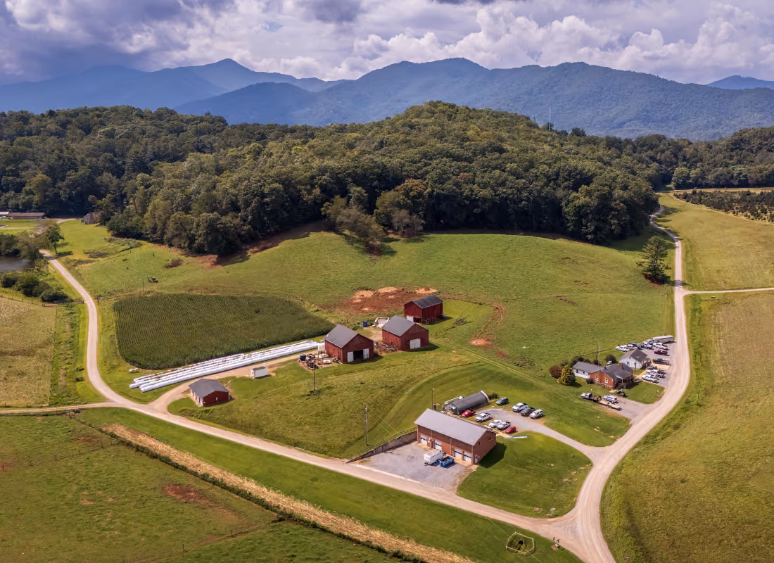 Aerial view of a rural Appalachian farm community surrounded by forested mountains, representing counties served by the ARC POWER Initiative