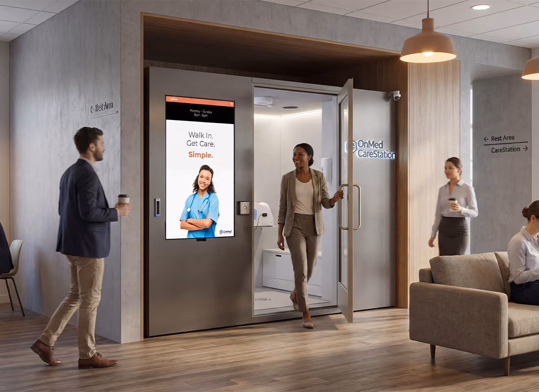 People walking through an office lobby past an OnMed CareStation™ with a woman exiting through the open door
