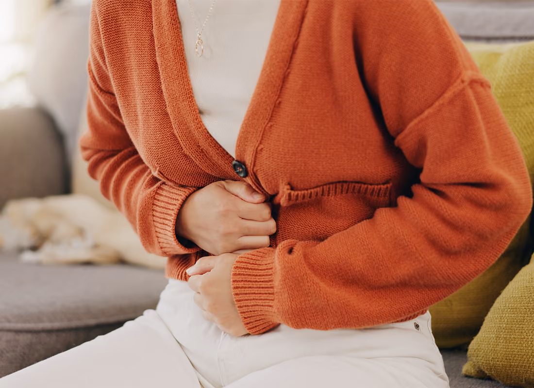 Person seated on a couch holding their stomach in discomfort