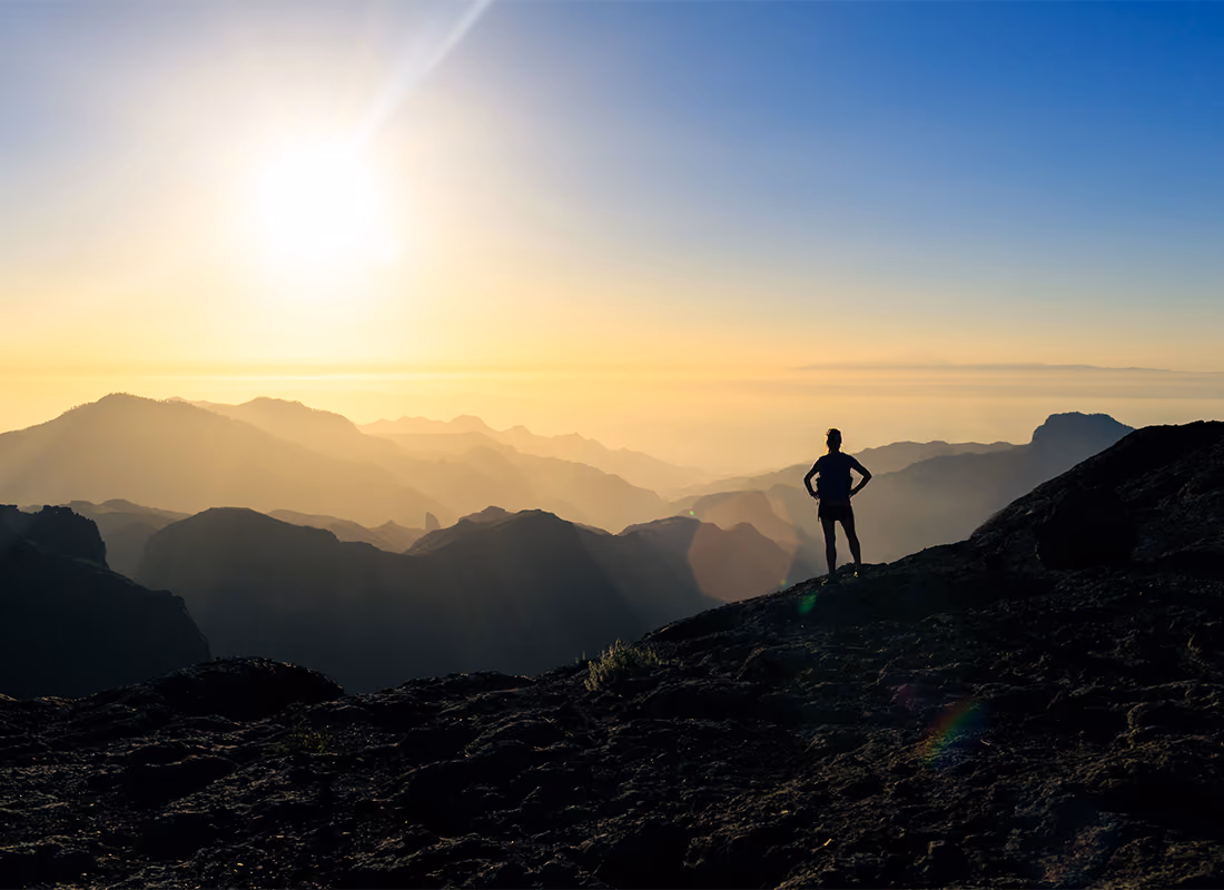 Silhouette of a person standing on a mountain ridge at sunrise overlooking a layered mountain range