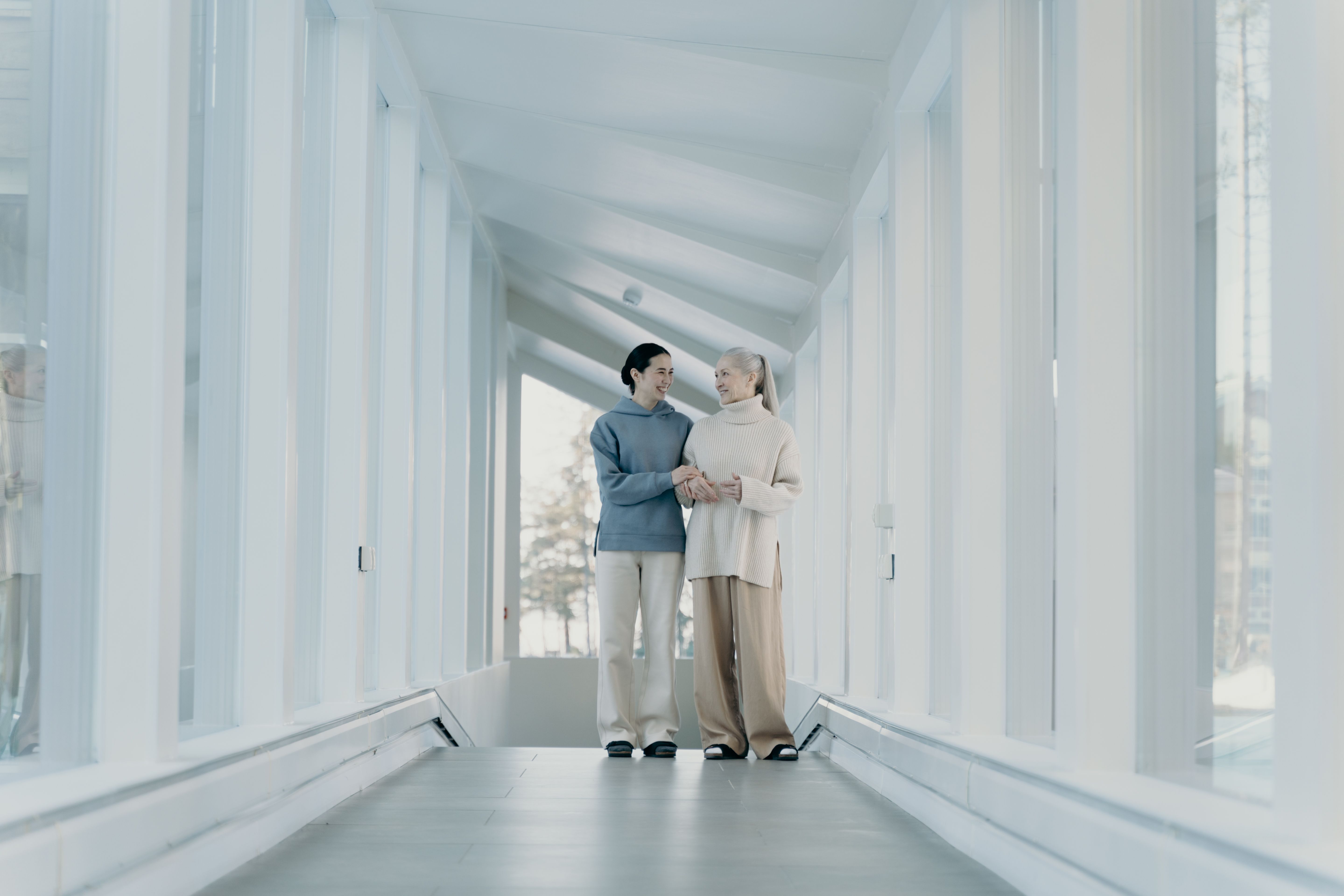 Two women walking arm in arm together down a sunlit hallway, representing guided care navigation and support.