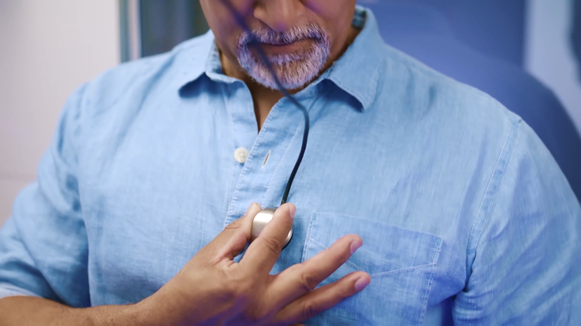Close-up of a man using a wearable digital stethoscope device on his chest, representing remote chronic condition monitoring.