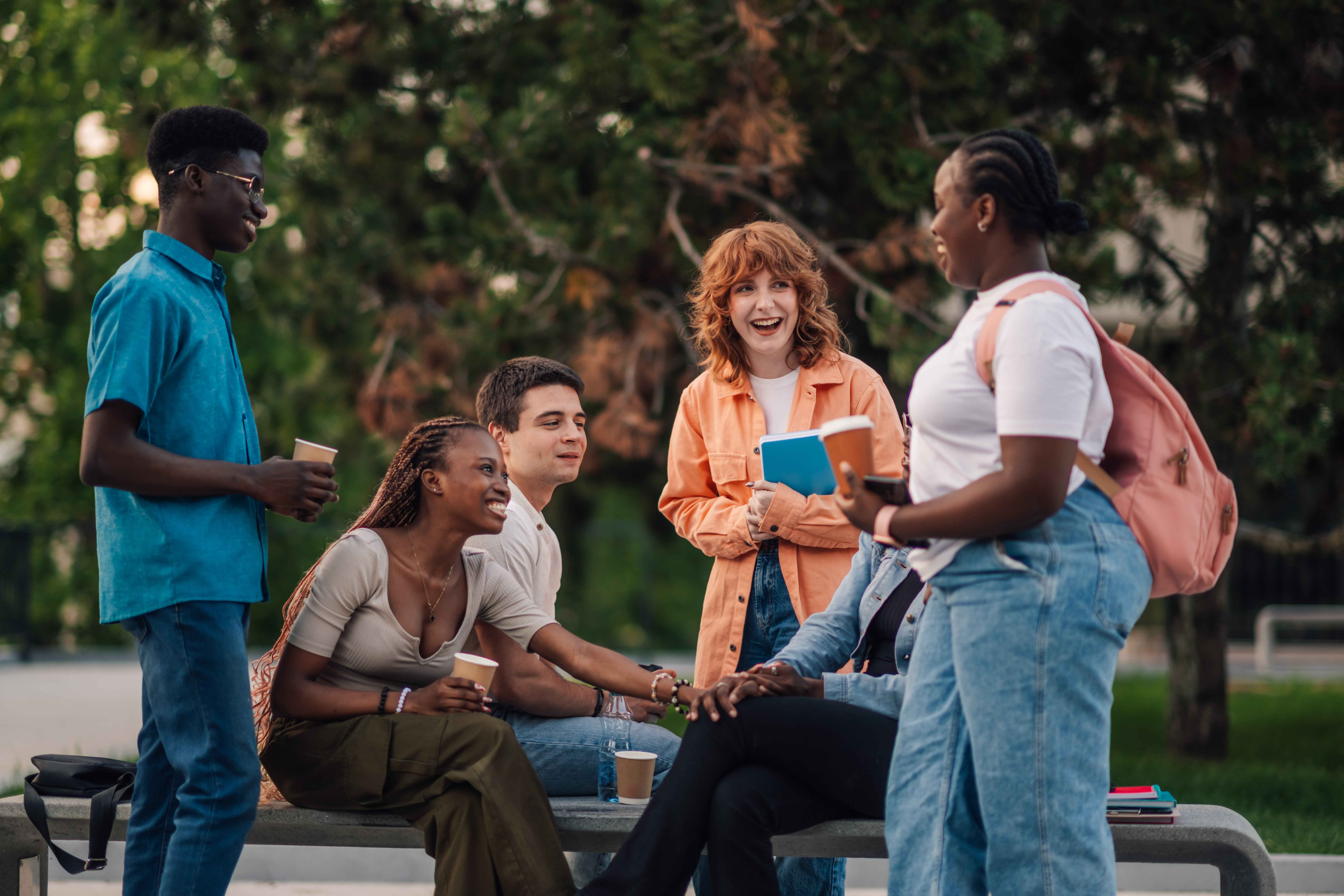 Group of college students laughing together outdoors on a campus bench, representing the residential life community ACUHO-I supports.