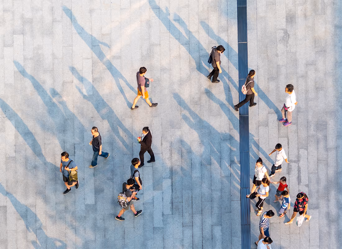 Aerial view of pedestrians walking across a paved plaza, casting long shadows