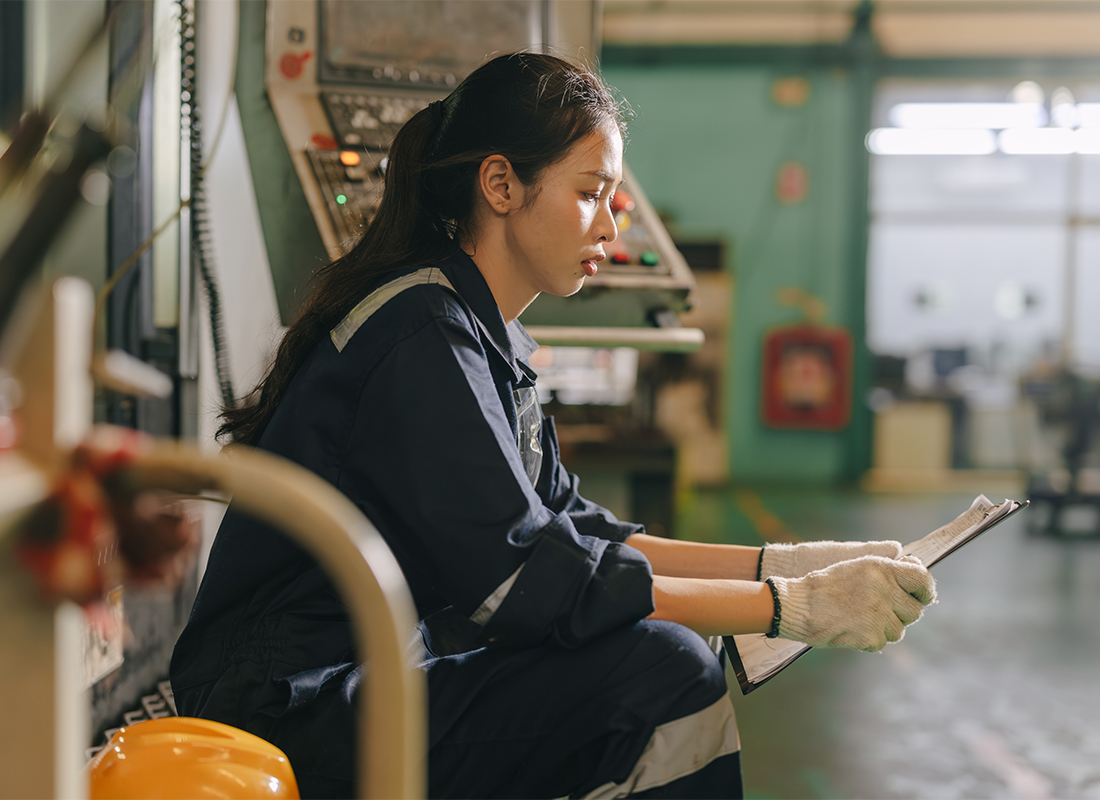 Factory worker in safety gear reviewing a clipboard checklist on the production floor.