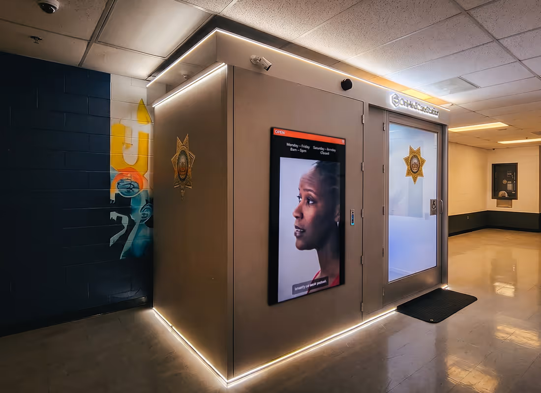 OnMed CareStation® health kiosk installed in a correctional facility hallway, displaying open hours and a live provider on screen
