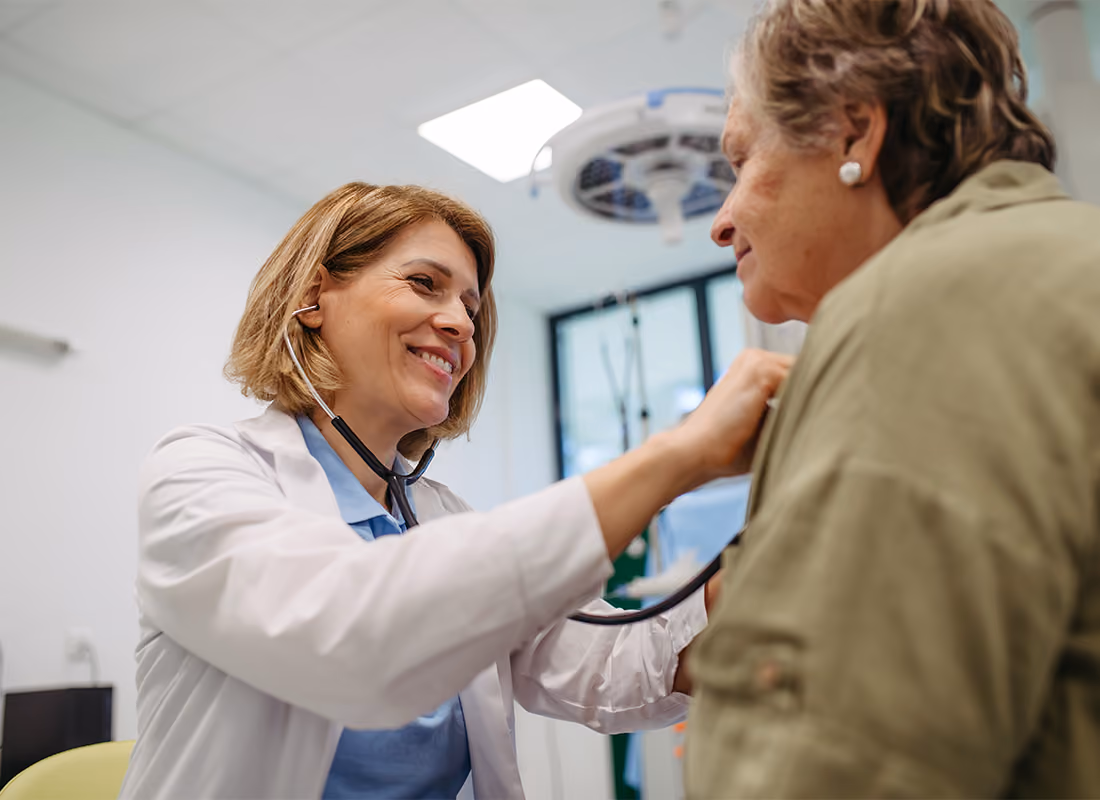 Doctor listening to an older patient's heartbeat with a stethoscope in an exam room