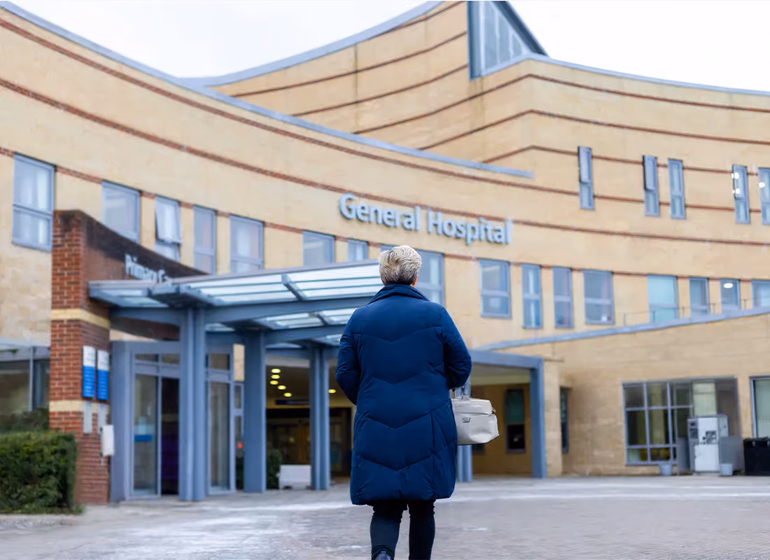 Person in a dark blue puffer coat walking toward the entrance of a General Hospital building