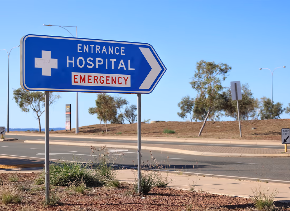 Blue road sign pointing to the hospital emergency entrance along an empty roadway