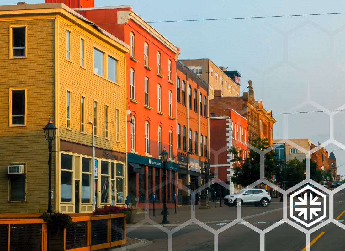 Small-town main street at golden hour lined with colorful brick and wood-sided storefronts, with a car parked near the corner