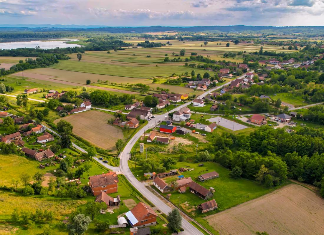 Aerial view of a rural village with scattered homes, farm fields, and a winding road surrounded by green countryside