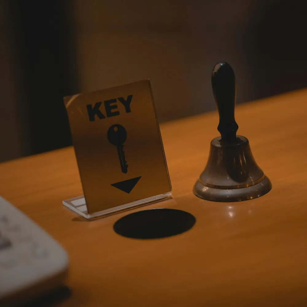 Small sign with a key icon and the word 'KEY' next to a service bell on a wooden counter.