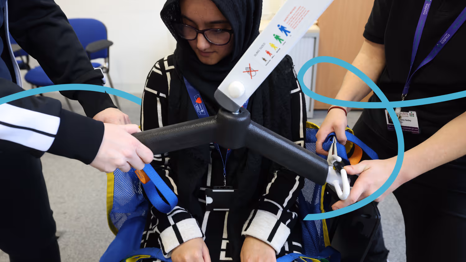 Two Routes Healthcare staff members practise fitting a hoist sling during a hands-on training session, with a trainer guiding the process.