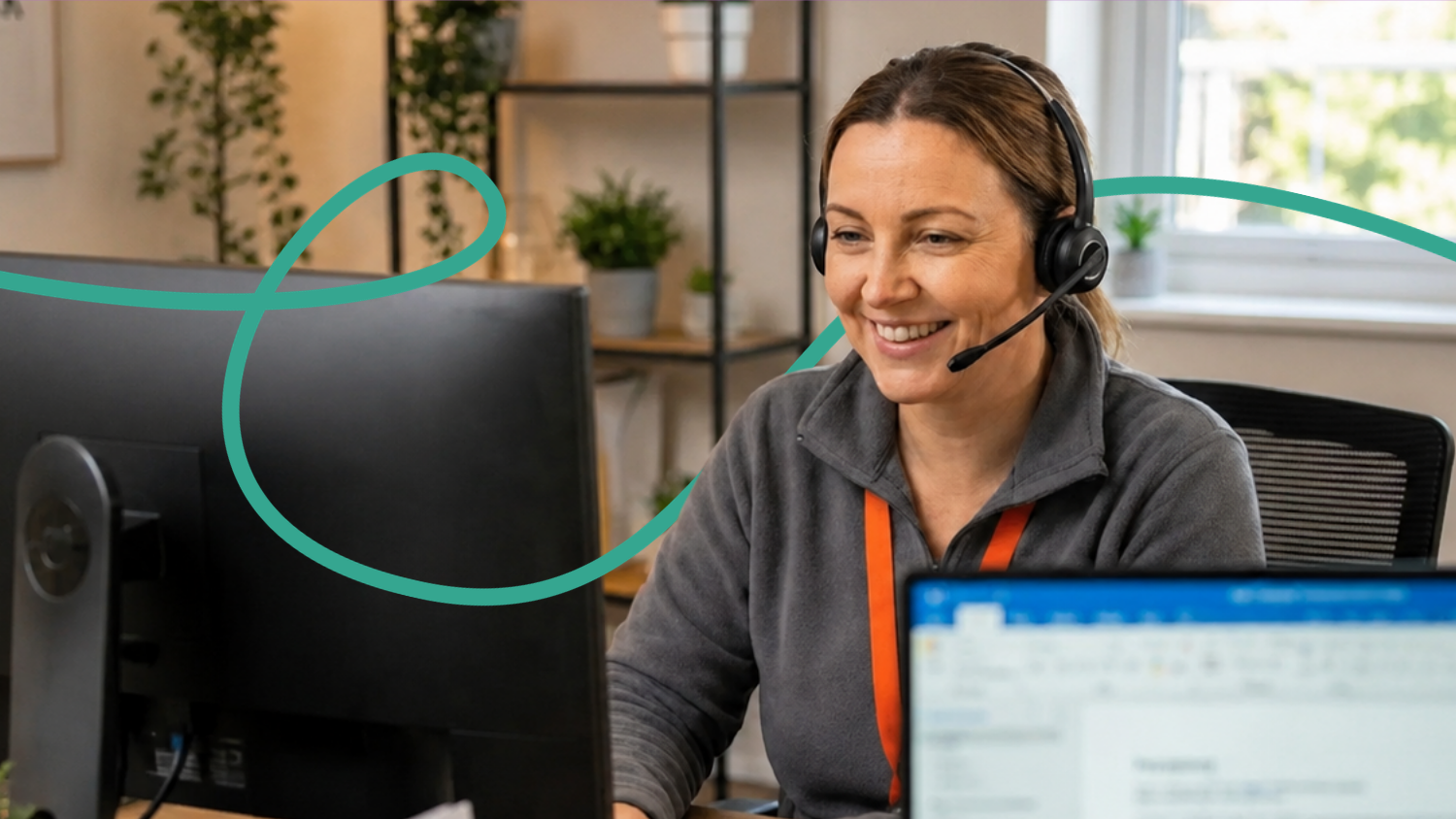 A Routes Healthcare care coordinator wearing a headset smiles while working at her desk in the office.