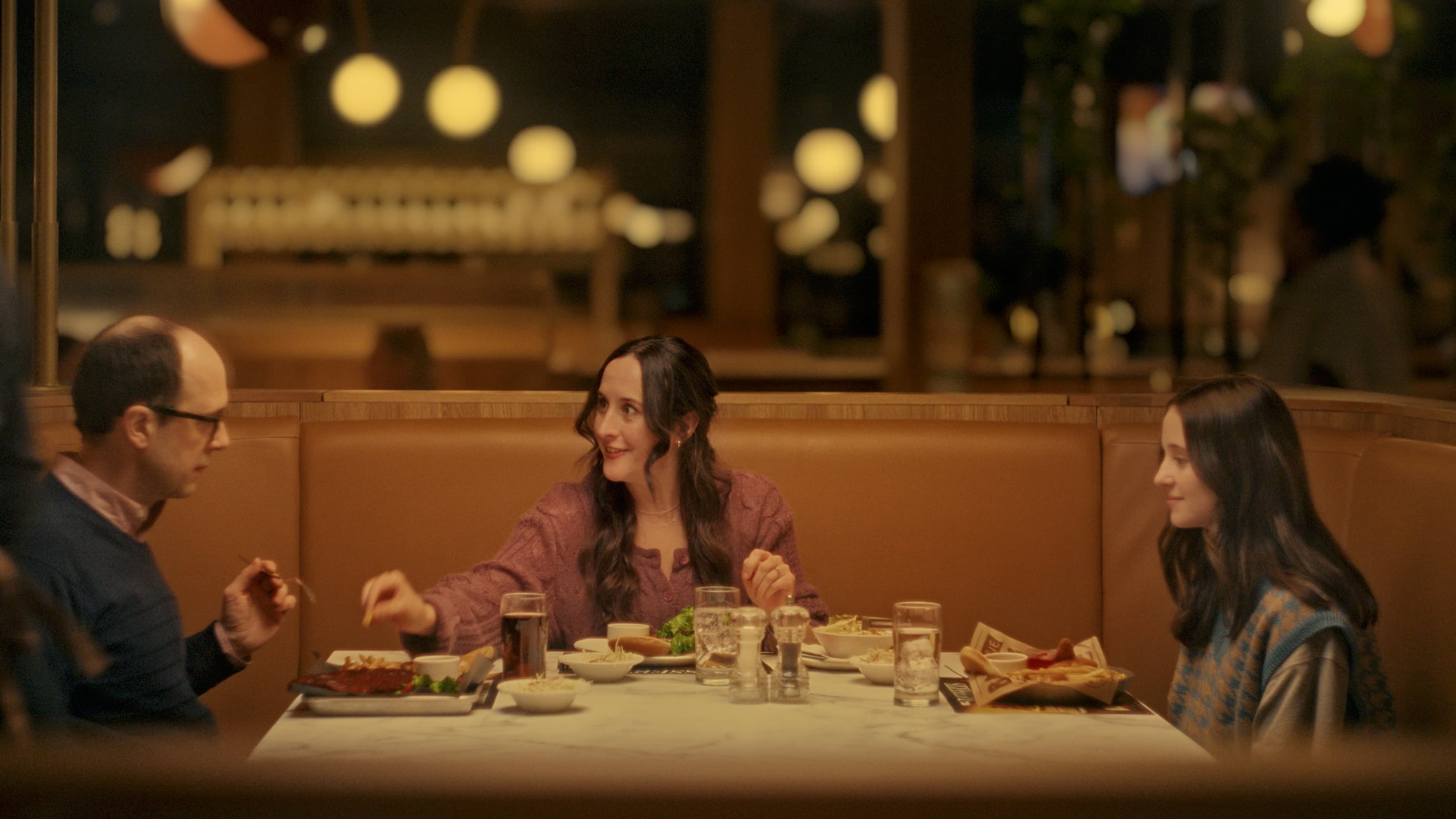 Trois personnes assises à une table de restaurant avec repas dans un cadre chaleureux et lumineux.