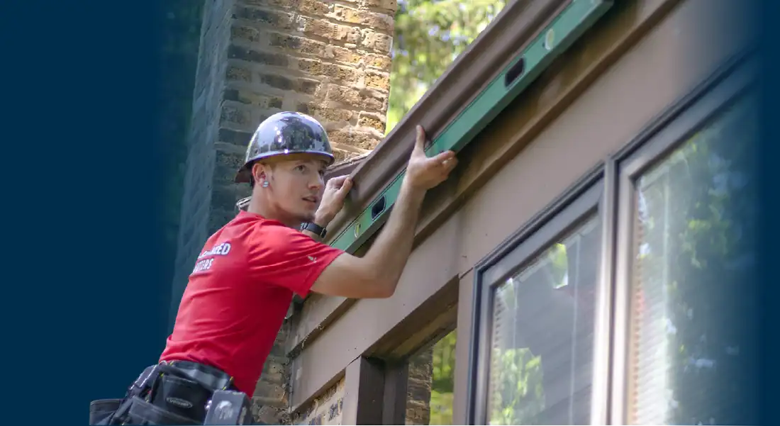 Worker wearing a helmet uses a level tool to check if the gutter he is installing is correctly leveled