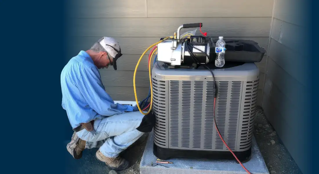 Technician kneeling and working on an HVAC unit outside a house with tools and hoses attached.