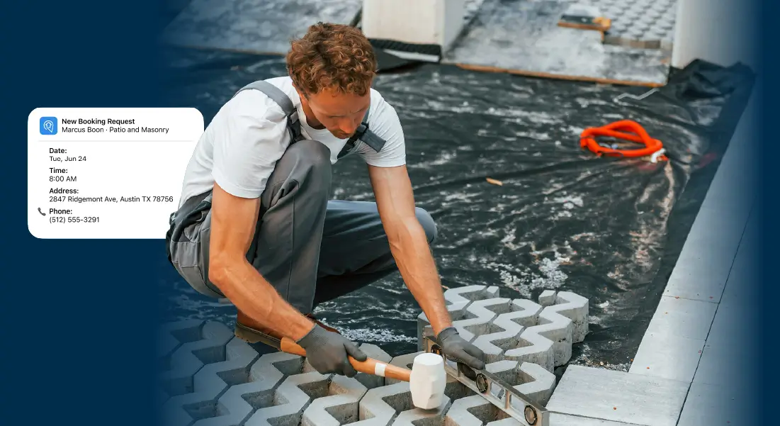Worker installing interlocking concrete pavers on a patio using a hammer and level. A SignpostAI Smart Booking notifications indicates he has booked a job while he's been working